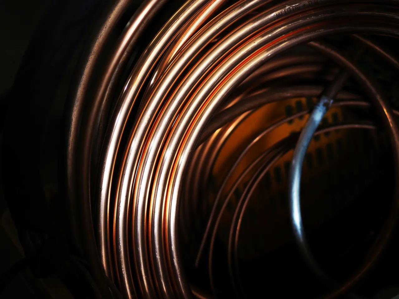 Spiralfoermig gewickeltes Kupferrohr in Nahaufnahme vor dunklem Hintergrund.